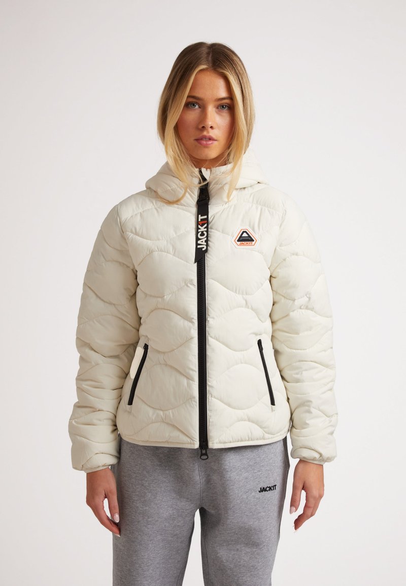 Vadderad krämfärgad jacka med huva, med ett zigzag-quiltrat mönster, framzipper och logotypdetalj på bröstet. Matchas med gråa sweatpants.