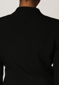 Svart blazer med en figurnära passform, slät textur och klassisk krage. Baksidan visar upp rena linjer med en enkel söm.