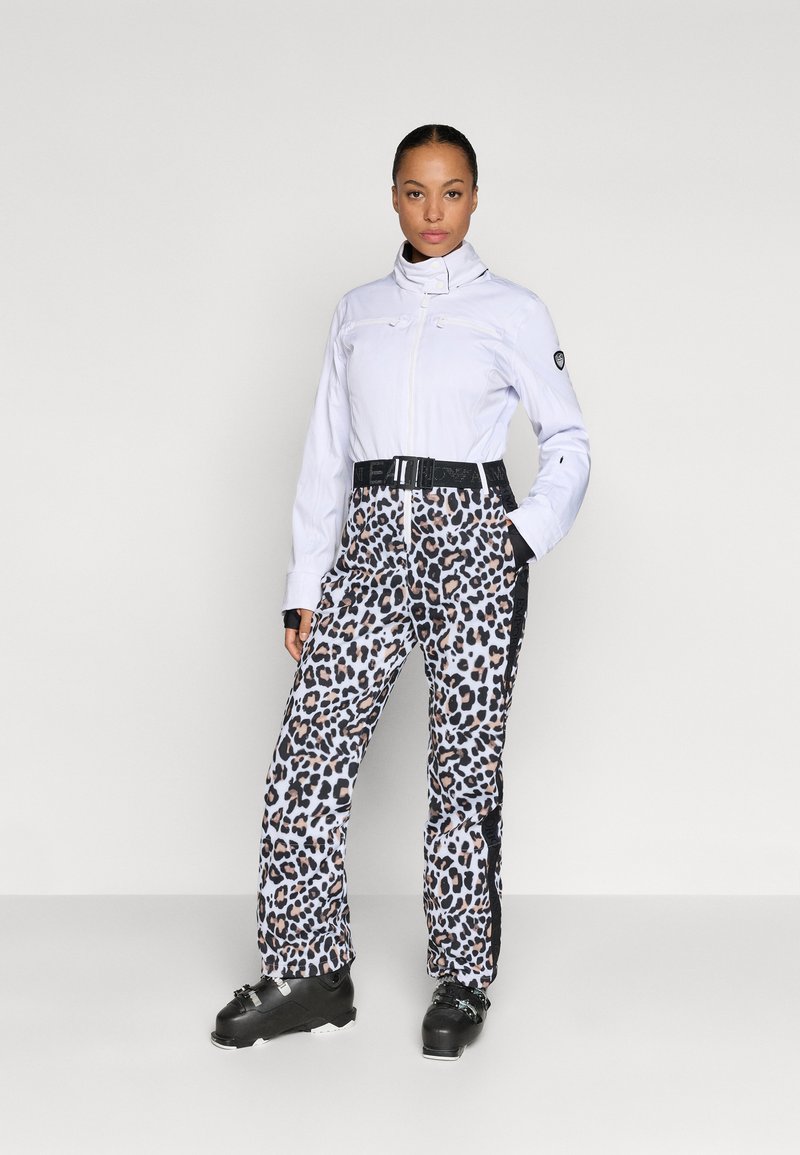 Îmbrăcăminte de schi care include o jachetă albă și pantaloni cu imprimeu leopard, accesorizați cu o curea neagră. Materiale texturate, un design elegant și modele în contrast.