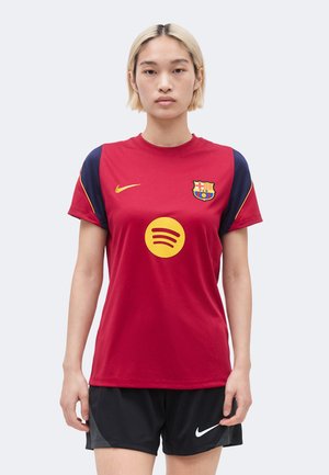 Personne portant un maillot de football FC Barcelone rouge et bleu marine avec les logos jaunes Nike et Spotify, associé à un short Nike noir, debout droit.