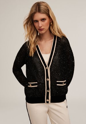 Cardigan noir en tricot avec des détails métalliques, un bord beige en contraste, deux poches avant et des boutons dorés. Coupe décontractée.