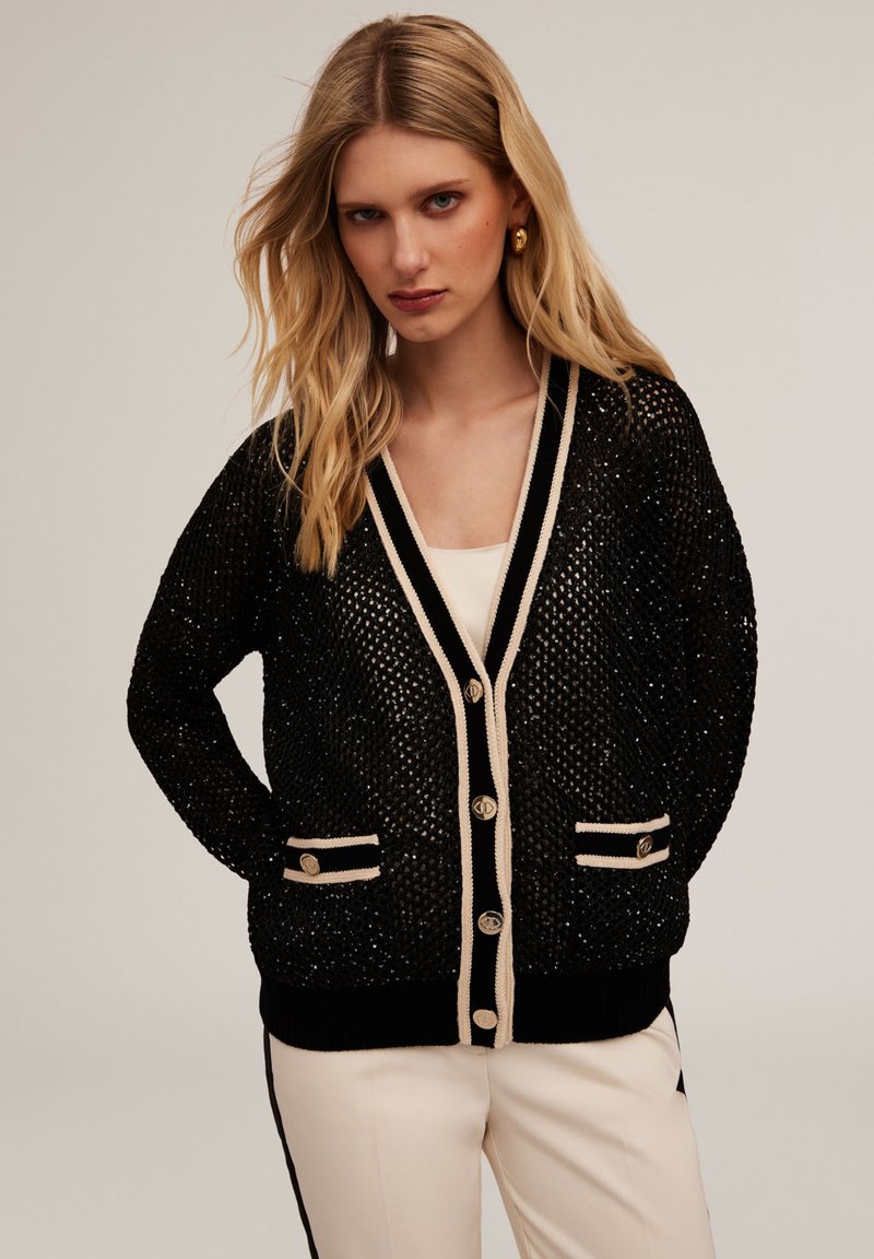 Cardigan nero lavorato a maglia con dettagli metallici, bordi beige a contrasto, due tasche frontali e chiusure con bottoni dorati. Vestibilità casual.