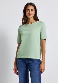Haut à manches courtes, vert clair, en tissu doux avec un col rond et une coupe décontractée, associé à un jean en denim bleu. Design simple et polyvalent.