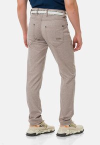 Hellgraue, strukturierte Hose mit Slim-Fit-Schnitt, ausgestattet mit Gesäßtaschen und einem gemusterten weißen Gürtel. Tragen mit beigen Sneakers.