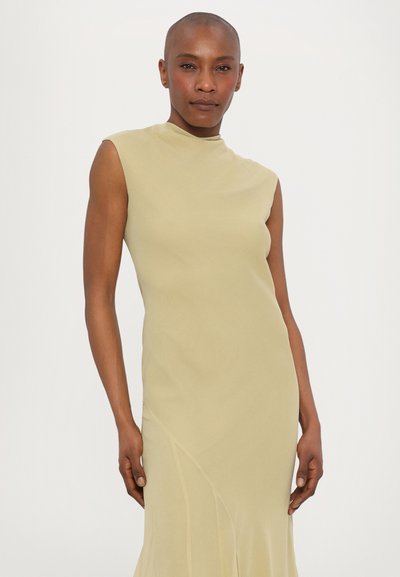 Mouwloze midijurk van zacht, lichtgroen stof. Heeft een hoge hals en een vloeiende silhouette met details in de zijnaad. Soepele textuur.