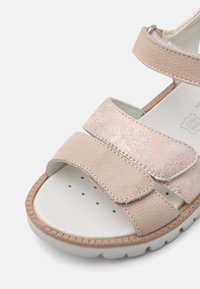 Lys beige sandaler med tre justerbare stropper, som har en metallisk detalj, teksturert skinnfinish og en polstret såle med perforeringer.