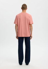 Ροζ βαμβακερό μπλουζάκι σε άνετη γραμμή, με κοντά μανίκια και στρογγυλή λαιμόκοψη, συνδυασμένο με σκούρο τζιν και μαύρα παπούτσια.