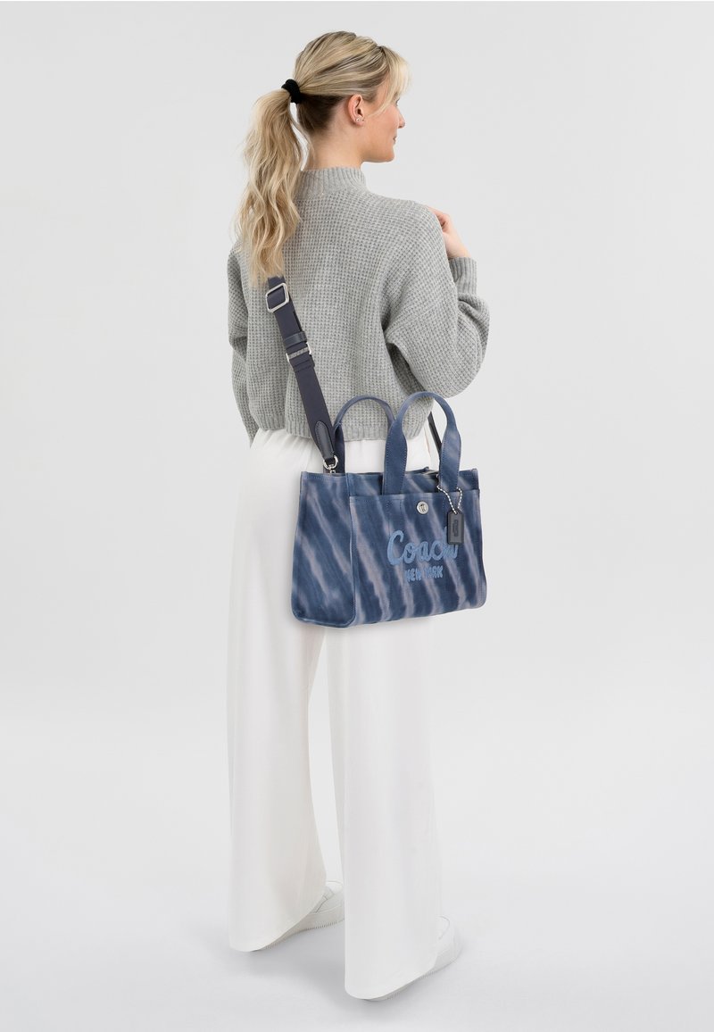 Blue canvas handbag with a tie-dye pattern, two handles and a detachable shoulder strap, featuring the logo "Coach New York" on the front.