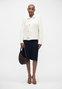 White fluffy tailored jacket with a collar, brown buttons; navy knit skirt, brown shoulder bag, and transparent high-heeled shoes.