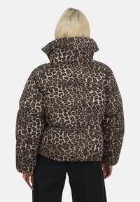 Puchowa kurtka z wysokim kołnierzem, ozdobiona wzorem w panterę w odcieniach beżu i czerni. Miękka tekstura, pudełkowy kształt i szerokie rękawy.