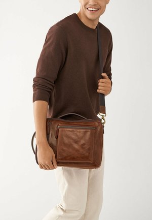 Sac messager en cuir marron avec une poche zippée à l'avant, une bandoulière et une poignée supérieure, présentant une texture lisse et un design minimal.