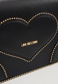 Černá kožená kabelka s designem srdce, zdobená zlatými hroty a zlatým logem "LOVE MOSCHINO" na přední straně.