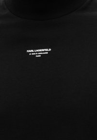 Μαύρο ύφασμα με λευκό κείμενο «KARL LAGERFELD 21 RUE ST-GUILLAUME PARIS» στο κέντρο κοντά στην κορυφή.