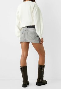 Sweatshirt oversize blanc, mini-jupe en denim gris, ceinture cloutée noire et bottes vertes arrivant au genou avec des accents de boucle.