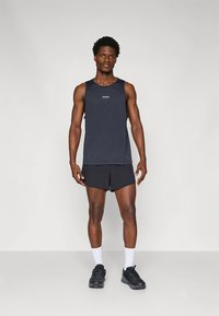 Maiou sport fără mâneci, bleumarin, cu logo, asortat cu pantaloni scurți negri. Modelul poartă șosete sport albe și adidași negri.