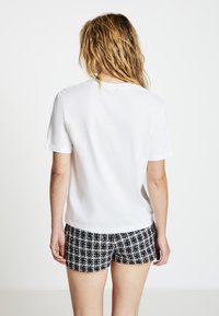 Weißes T-Shirt mit kurzen Ärmeln und Rundhalsausschnitt, kombiniert mit schwarz-weiß gemusterten Shorts mit einem Gitterdesign in verschiedenen Farbtönen.