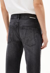 Zwarte denim jeans voor heren hebben een rechte pasvorm, kenmerkende achterzakken en een gestructureerde stof met een subtiel vervaagd patroon.