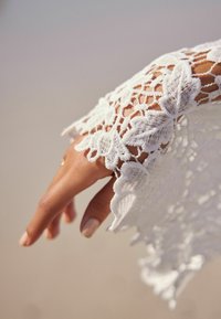 Biała koronkowa rękawka z misternymi wzorami kwiatowymi, z falbaniastymi brzegami i lekką teksturą, opadająca na dłoń.