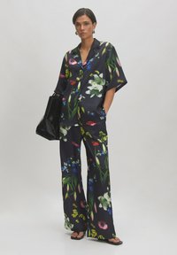 Bloemmotief set bestaande uit een losse korte mouwen blouse en wijde broek van zwarte stof. Geaccentueerd met levendige kleuren en texturen.
