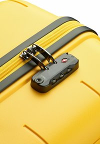 Maleta rígida amarilla con una superficie texturizada, cremallera negra y un candado de combinación aprobado por la TSA, que presenta tres diales y un agujero para llave.