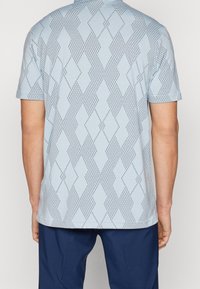 Polo bleu clair à manches courtes, avec un motif en diamant texturé et de subtils points noirs. Col arrondi et ourlet droit.