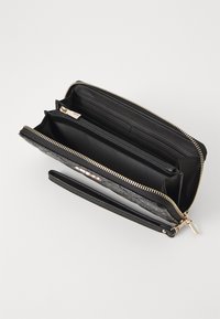 Portafoglio nero in pelle con un esterno testurizzato, zip dorata, più slot per carte, un compartimento con zip e una tracolla.