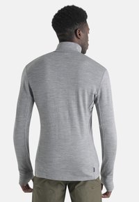Light gray long-sleeve shirt with a high collar, made of smooth fabric. Features fitted design and thumbholes at sleeve cuffs.