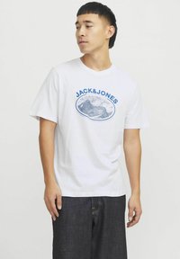 Hvid bomulds t-shirt med et blåt grafisk tryk, der viser "JACK&JONES" og bjergmotiver. Korte ærmer, rund halsudskæring, afslappet pasform.