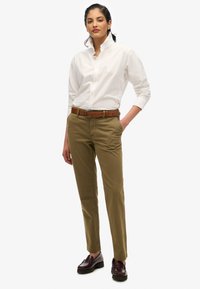Chemise blanche à col haut, chinos beige, ceinture marron et chaussures en cuir foncé. Design simple, coupe classique et couleurs neutres.