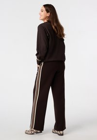 Sweatshirt marron à coupe décontractée, accompagné d'un pantalon marron avec des rayures verticales crème, beige et marron foncé. Des chaussures à imprimé animal viennent compléter la tenue.
