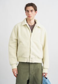 Ζακέτα από φλις εκρού με γιακά, ριγωτές μανσέτες και τελείωμα. Διαθέτει πλαϊνές τσέπες και μικρό λογότυπο στο στήθος.