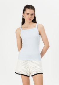 Lyseblå ribbet tanktop med firkantet hals og tynne stropper, kombinert med hvite mønstrede shorts med svart bølgete kant.