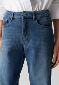 Jeans in denim di blu medio, design a cinque tasche, gamba dritta, chiusura a bottone e dettagli di cucitura in contrasto sulle tasche.