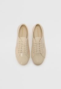 Beige blanke sneakers med snørebåndsdesign. Glatt overmateriale, rund tå og strukturert gummisåle. Merking synlig på siden.