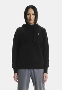 Mustmust sooviga kapuutsiga, ees taskuga ja nööridega, millel on rindkere kohal väike valge logo. Pehme, sile kangas, mugav lõige.