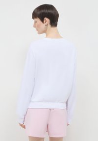 Felpa bianca a maniche lunghe realizzata in tessuto morbido, con scollatura rotonda e polsini a costine, abbinata a pantaloni corti rosa chiaro.