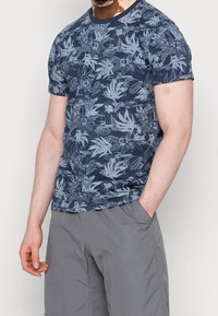 Navy blue t-shirt featuring a light gray floral pattern, short sleeves, round neckline, and a fitted cut. Worn with gray shorts.
