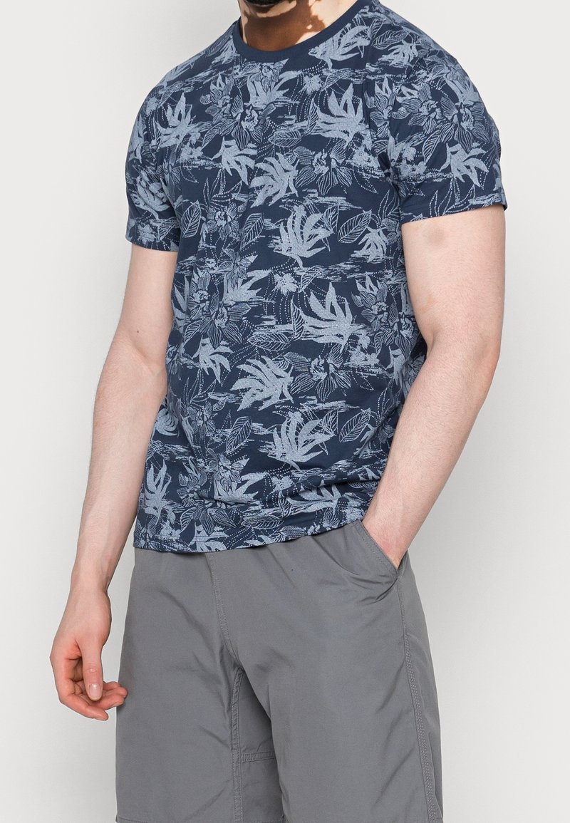 Navy blue t-shirt featuring a light gray floral pattern, short sleeves, round neckline, and a fitted cut. Worn with gray shorts.