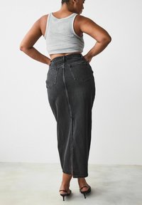 Sort denim midi-nederdel med slids i midten bag, høj talje-design og to baglommer, sammen med en grå tanktop og sorte hæle.