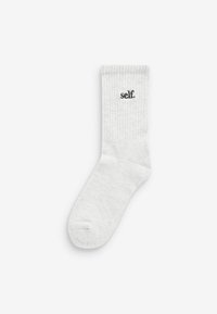 Hvid bomuldsstrømpe med ribbet tekstur og et sort broderet logo, der læser "self." placeret på siden.