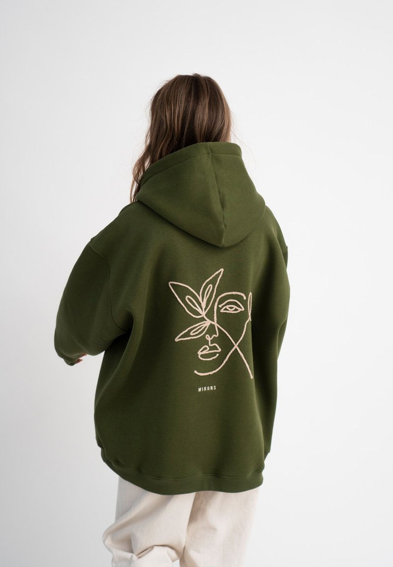 Hoodie vert olive au design surdimensionné. Présente un dessin linéaire minimaliste d'un visage et de feuilles au dos. Tissu doux et texturé.