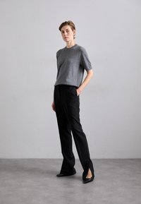 Szürke kötött, rövid ujjú pulóver fekete, szabott nadrággal, amelynek oldalán hasíték található, kiemelve a hegyes orrú fekete magassarkúval. Simára kidolgozott textúra.