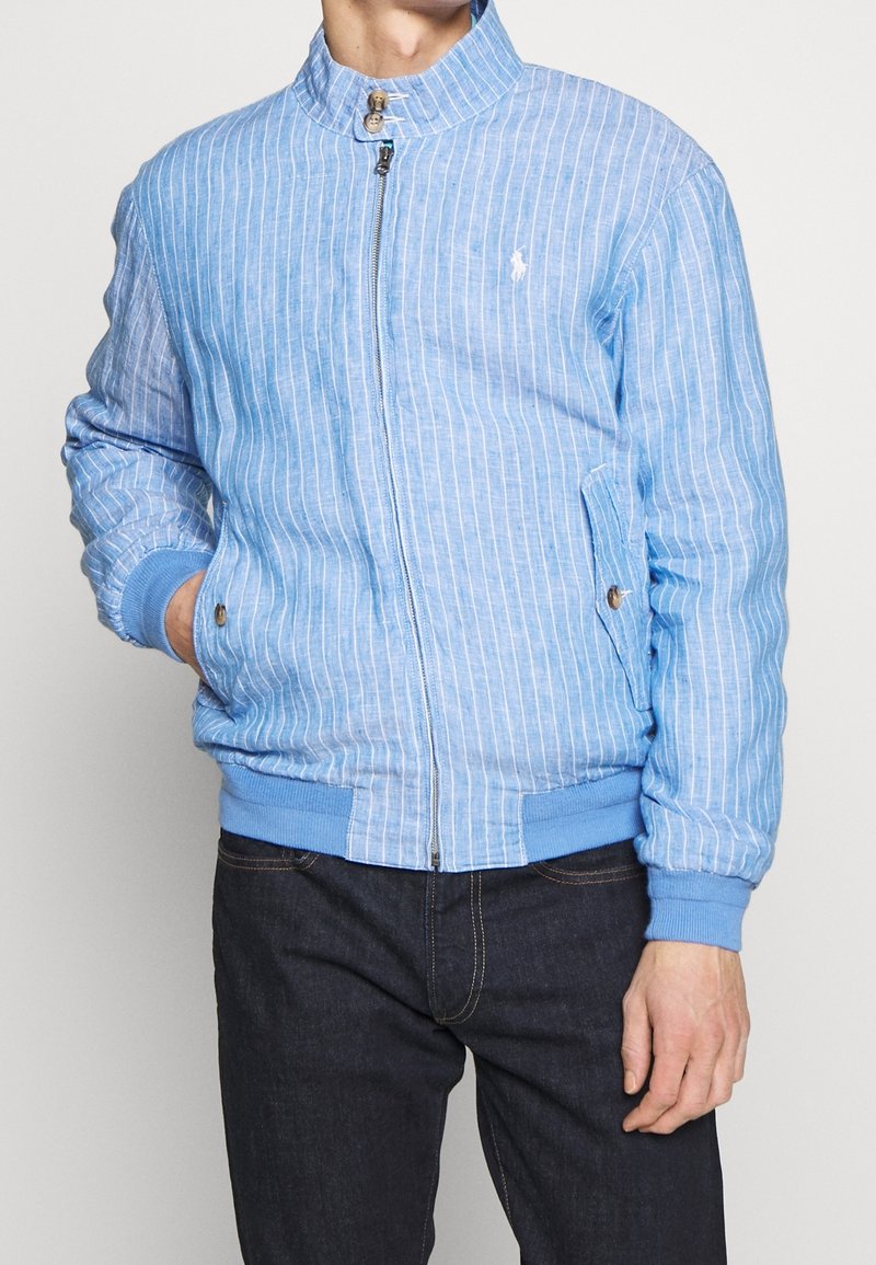 Ljust blå randig bomberjacka med hög krage, dragkedjestängning och elastiska manchetter. Har sidofickor och kontrasterande blå midjeband.