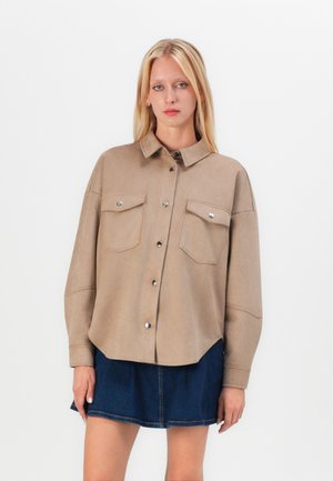Beige skjorte med knapper lavet af blødt materiale, med to forlommer, sølvdetaljer og en afslappet pasform, parret med en mørk denimnederdel.