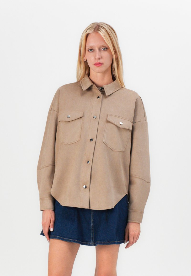 Beige button-up shirt gemaakt van zacht materiaal met twee borstzakken, zilveren hardware en een relaxte pasvorm, gecombineerd met een donkerdenim rok.