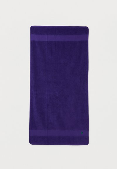 Βαθυμωβ ορθογώνια πετσέτα με δύο πιο σκούρες μοβ λωρίδες κοντά στις άκρες και μικρό πράσινο κεντημένο λογότυπο στην κάτω δεξιά γωνία.