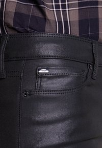 Černé džíny z denimu s klasickým pětiprvkovým designem kapes, hladkou texturou a malou kovovou značkou na zadní kapse.