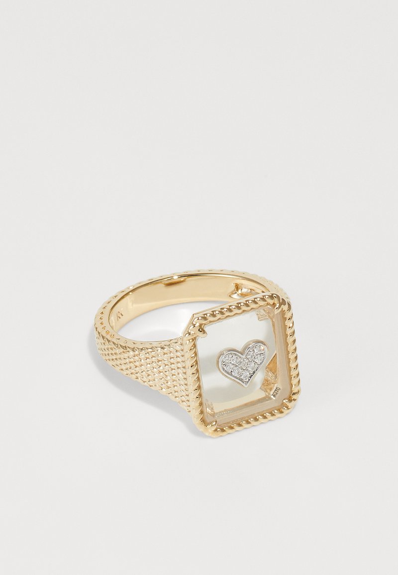 Arany gyűrű texturált sávval, négyzet alakú, átlátszó középponttal és benne egy kis gyémánttal díszített szív mintával.