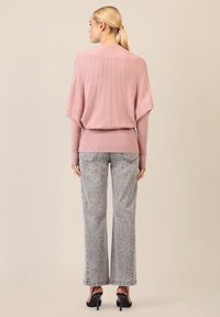 Hellrosa gerippter Pullover mit Fledermausärmeln, kombiniert mit hellgrauen Jeans mit blauen Punktmustern. Schwarze High Heels vervollständigen das Outfit.