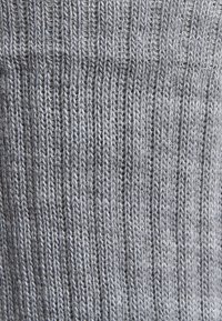 Tela de punto gris con una textura acanalada, que presenta hilos finos y un cosido uniforme. Apariencia suave, con un ligero brillo.